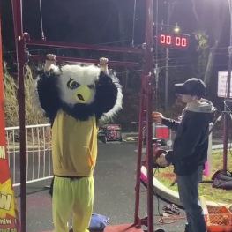Owl mascot holding onto a carnival pull-up machine, man next to the owl operating the machine. 